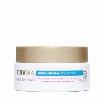 Embalagem tipo pote do Creme hidratante facial fortalecedor da linha Hidra Mineral da Eudora. Embalagem branca com tampa de rosquear dourada na parte superior, rótulo em tons de verde, vermelho e dourado no fundo branco.