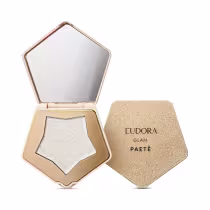 O produto apresentado é um item de maquiagem da marca Eudora, da linha Glam. Trata-se de um Iluminador com espelho, em formato pentagonal, com uma estrutura dourada. Dentro, há um pó iluminador prateado e espelho na parte interna da tampa.