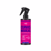 Frasco de spray rosa com rótulo roxo e azul contendo "Curvas Mágicas", um produto de cuidados capilares da marca Widi Care, com informações sobre sua fórmula revitalizante.