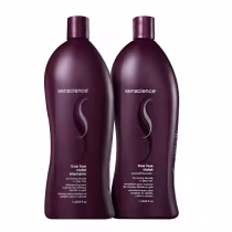A imagem mostra dois frascos de plástico roxo escuro de shampoo e condicionador da linha True Hue Violet da marca Senscience. Os frascos têm formato cilíndrico e tampas da mesma cor. Nas embalagens, há o logotipo da marca em branco e as descrições.