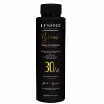 A imagem mostra a embalagem preta da água oxigenada posicionada sobre uma pedra clara, em um fundo bege, com folhas verdes decorando a cena, transmitindo uma atmosfera natural para esse cosmético capilar.