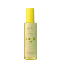 Perfume em spray em frasco cilíndrico amarelo. Embalagem transparente com rótulo dourado e texto "Skelt Unexpected Day Fine Fragrance". Descrição adicional em português: "Pera, Chantilly, Flor de Laranjeira".