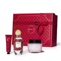 A imagem mostra um conjunto de produtos, com um frasco de eau de parfum, embalagem de creme hidratante corporal e creme para as mãos. O destaque é uma bela caixa de presente vermelha, com detalhes em relevo e um laço de fita vermelho.