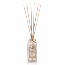 Difusor de aromas em frasco de vidro transparente com tampa dourada e laço de cetim bege. Rótulo com texto "Difusor de Aromas" e "Frutas Frescas". Hastes de madeira inseridas no frasco para dispersão do aroma.