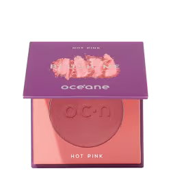 A imagem mostra o produto Blush Me da marca Océane. É uma embalagem quadrada de cor roxa que está semiaberta mostrando a cor do blush em um tom rosa com leve brilho perolado. A parte interna da embalagem é de cor pêssego claro,
