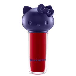 Produto de maquiagem em formato cilíndrico com a cabeça da personagem Hello Kitty como tampa. A parte superior é azul escuro com detalhes que representam os olhos, orelhas e laço da Hello Kitty. É possível ver a cor do produto pelo corpo transparente.