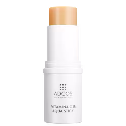Produto em formato stick, com embalagem cilíndrica branca. O rótulo na embalagem branca exibe o logotipo da marca Adcos e o nome do produto "Vitamina C 15 Aqua Stick". Na parte superior aparece um pedaço do produto em cor amarelo alaranjado.