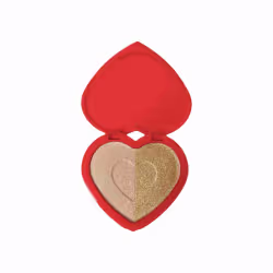 O produto apresentado é um iluminador em formato de coração, com uma embalagem vermelha brilhante. A parte interna do coração possui uma divisão, com uma metade em tom dourado e a outra em tom bege claro. Não há nenhum texto ou rótulo visível na imagem.
