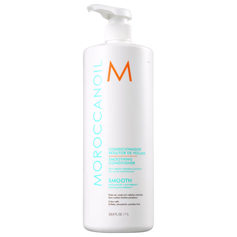 A imagem mostra o Condicionador Moroccanoil Smoothing 1L. O frasco é branco, com capacidade de 1 litro, e tem uma bomba dosadora na parte superior para facilitar a aplicação. O design é minimalista, com o nome da marca em laranja e detalhes em azul claro.