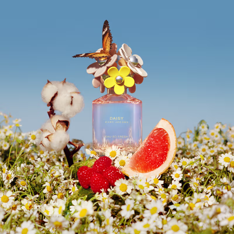 Frasco de perfume rosa da linha Daisy Marc Jacobs, com tampa decorada com flores amarelas e brancas. Rótulo com o nome da fragrância "Daisy Marc Jacobs Eau So Fresh" em letras douradas.