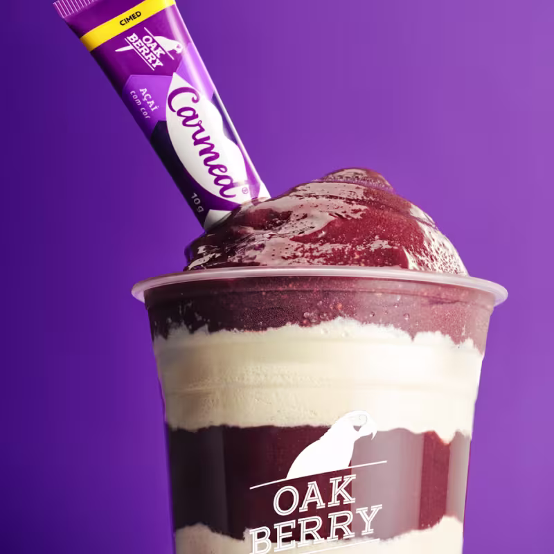 A imagem mostra um copo com açaí Oakberry e o Hidratante Labial Cimed Carmed Açai Oakberry.