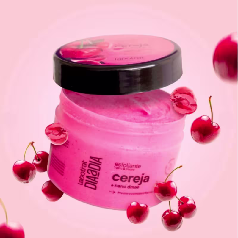 O produto apresentado é um esfoliante corporal da marca Labotrat, com o nome "Cereja" impresso no rótulo. A embalagem é um pote preto com tampa, e a cor predominante é o rosa. 300g.