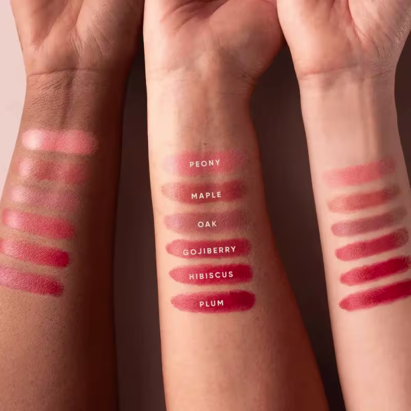 Imagem mostra diversos swatches de cores do blush Mascavo em tons de vermelho, rosa e roxo, com rótulos indicando os nomes das cores como Peony, Maple, Oak, Gojiberry, Hibiscus e Plum.