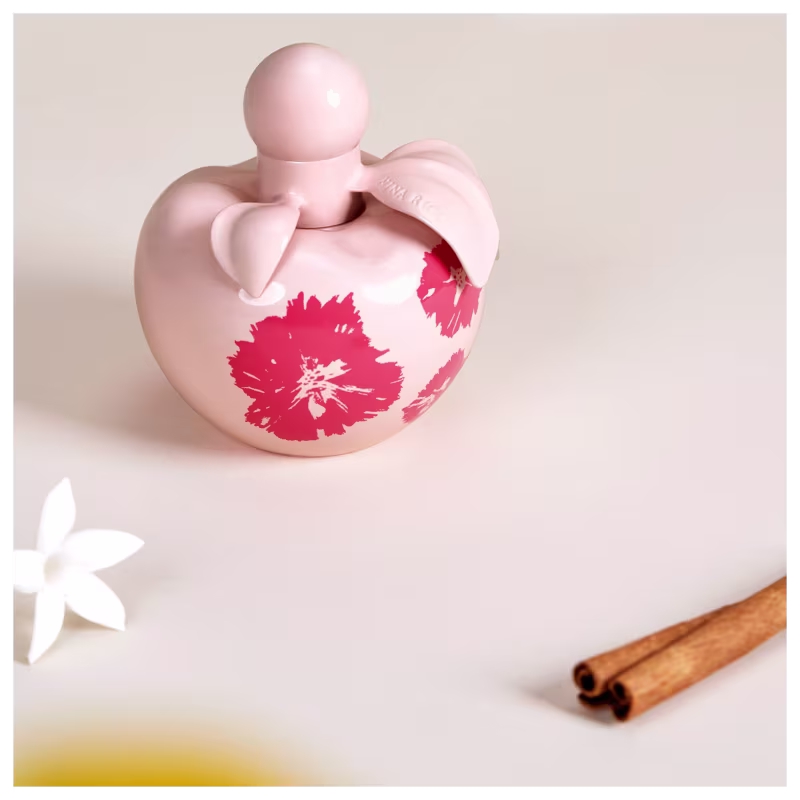 Conjunto de produtos Nina Ricci Nina Fleur. Frasco de perfume transparente em formato de coração com detalhes florais vermelhos. Loção corporal branca em tubo cilíndrico com o nome "Nina Fleur" impresso.