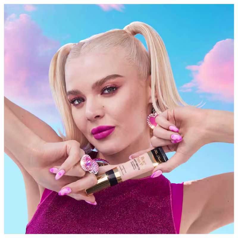 A imagem mostra uma mulher super produzida segurando uma embalagem da base próxima ao queixo.