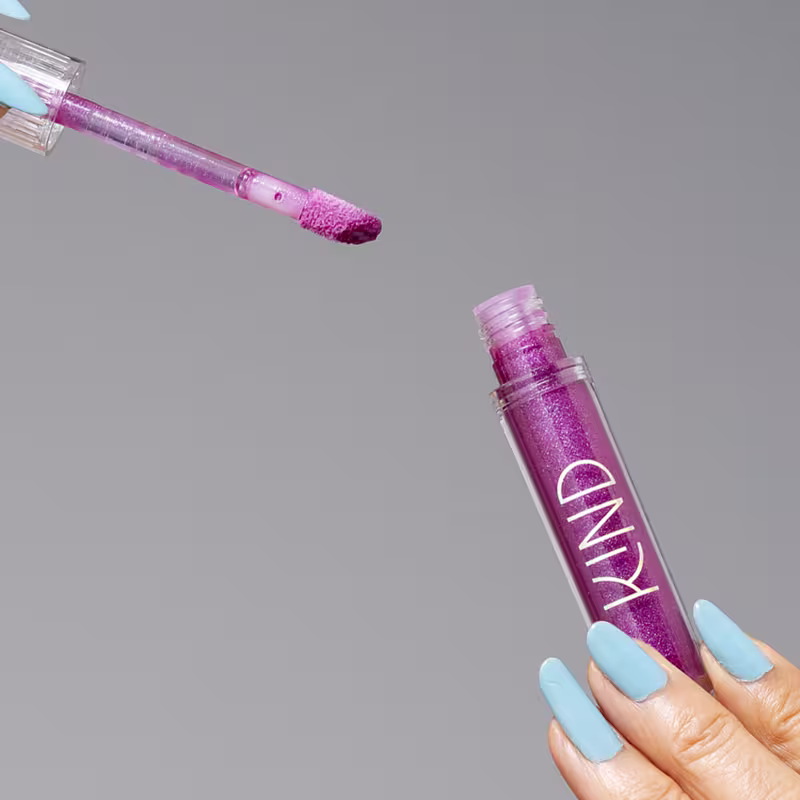 A imagem mostra a embalagem do gloss, aberta, sendo segurado por uma mão com unhas azuis.