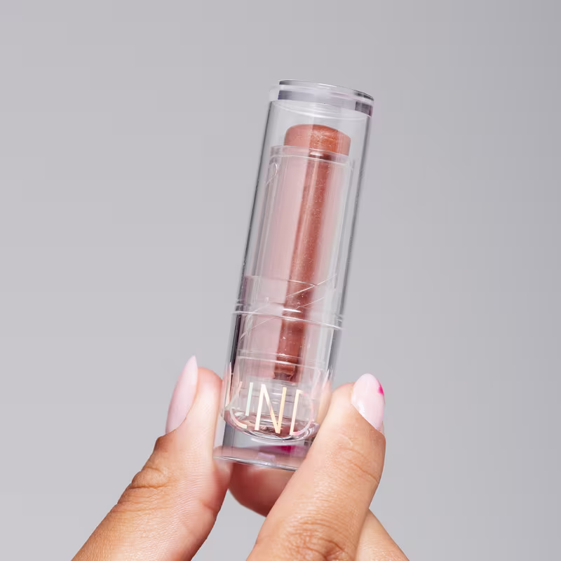 A imagem mostra a embalagem do balm, fechada, sendo segurado por uma mão negra.