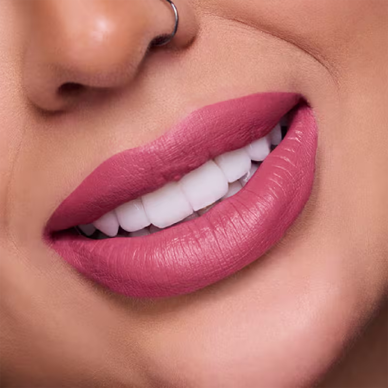 A imagem mostra um close nos lábios carnudos e bem delineados de uma mulher branca. Os lábios estão cobertos com o batom de tom rosa claro e mate, que realça a textura e o volume natural dos lábios.