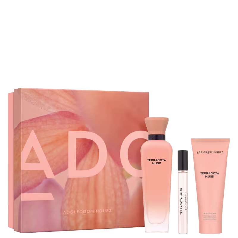 Conjunto de produtos lado a lado, com caixa quadrada rosa e imagem de flor e nome da marca em rosa. Frascos de perfumes, um com tampa de madeira e outro preto, vidro degradê transparente e rosa. Loção em embalagem rosa e escritos pretos.