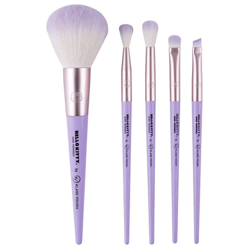 Pincéis com cabos plásticos lisos na cor lilás e detalhes metálicos rosados, variam em tamanho e formato, com cerdas sintéticas brancas. Um deles é maior, arredondado, provavelmente para pó. Os outros são menores, para sombras, delineadores e corretivos.