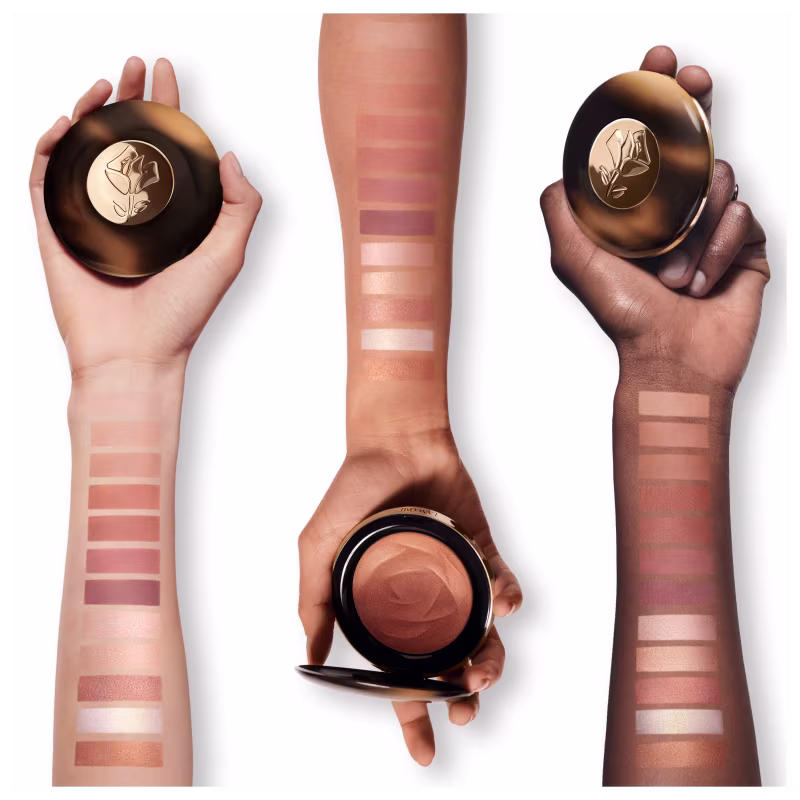 A imagem trás três embalagens com o iluminador. Elas têm formatos cilíndricos e são segurados por mãos femininas de diferentes tons de pele. No antebraço estão as tonalidades do iluminador e como eles ficam em cada pele.