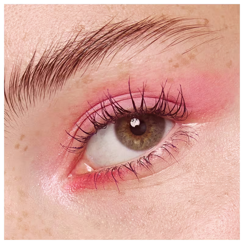 A foto mostra um rosto feminino branco aproximado, com foco no olho verde. A pálpebra está pintada com uma sombra  rosa claro e os cílios bem definidos e alongados.