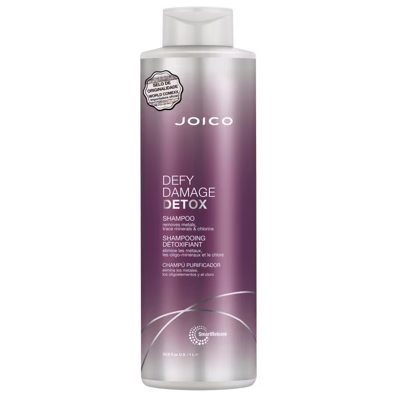 Shampoo detox Defy Damage da marca Joico. Embalagem cilíndrica roxa com detalhes prateados. Rótulo indicando que remove metais, minerais traço e cloro dos cabelos. Volume de 1L.