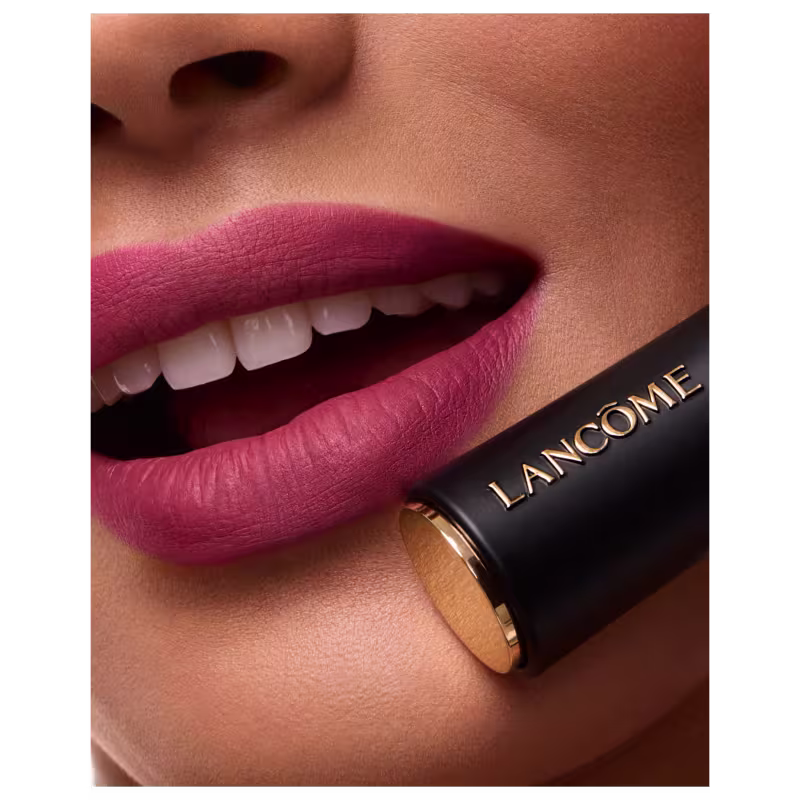 Imagem mostra um close-up dos lábios de uma modelo que está sorrindo e utilizando o batom rosado em seus lábios. Ao seu lado, segura a embalagem do batom próximo ao rosto.