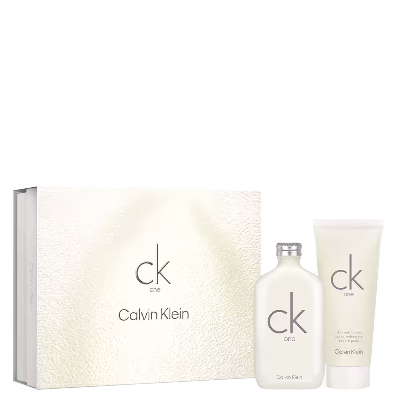 Um frasco de perfume transparente com tampa prateada e o logotipo "ck one" gravado no vidro. Uma caixa branca texturizada com o nome da marca "Calvin Klein" e o logotipo "ck one" em letras minúsculas cinza. Um tubo branco de loção corporal.