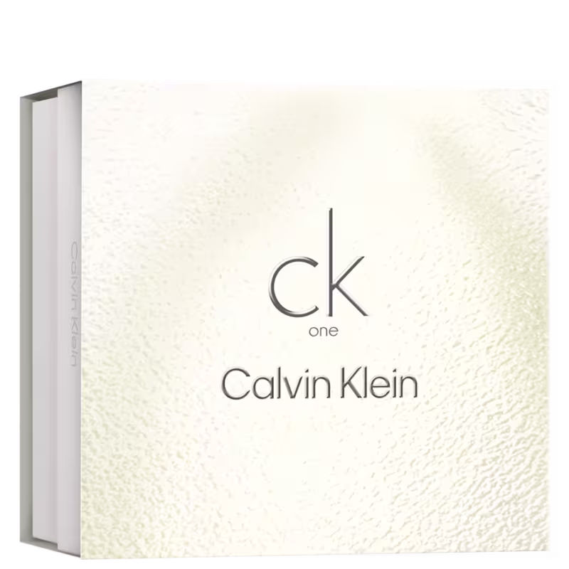 Caixa retangular branca com textura na superfície. Letras em cinza escuro "ck one Calvin Klein" estampadas na parte frontal. A embalagem tem um design minimalista e elegante, característico dos produtos da marca. As cores predominantes são branco e cinza.