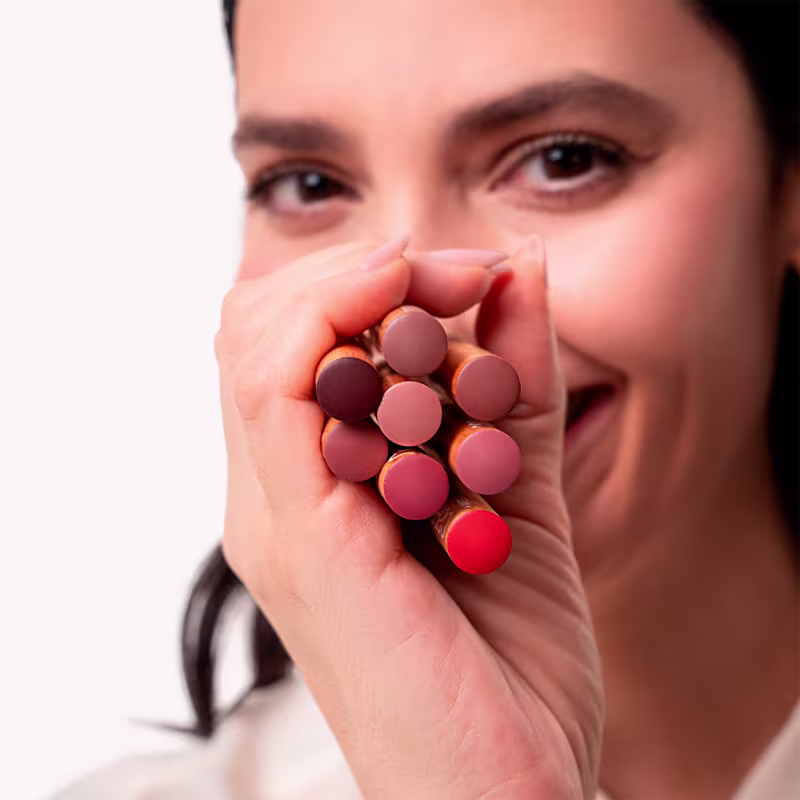 O produto visível é uma maquiagem para lábios. Consiste em várias pequenas esferas compactas de diferentes tons de rosa, variando do rosa claro ao vermelho vivo. As esferas estão agrupadas na palma de uma mão feminina.