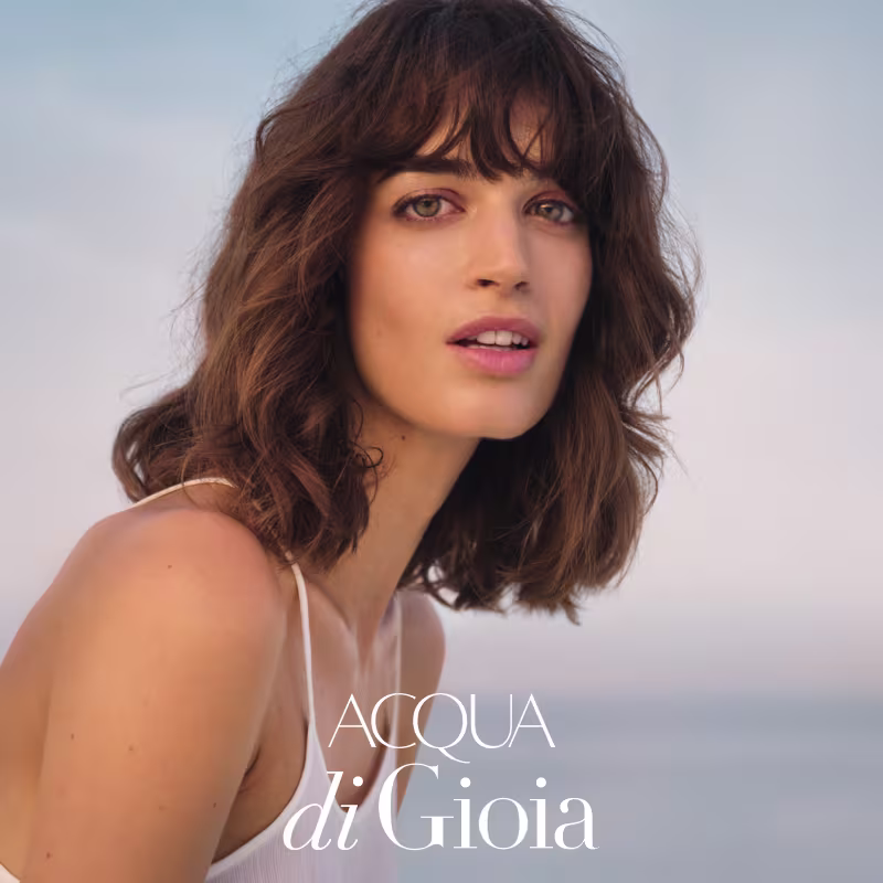 Uma modelo jovem de cabelo castanho escuro na altura do ombro sorri com uma expressão serena.