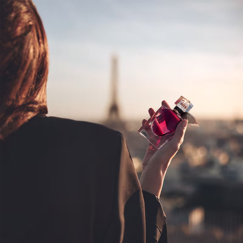 Perfume sendo segurado por uma modelo. Ao fundo, é possível ver a Torre Eiffel, um ícone da cidade de Paris, onde a marca Lancôme é sediada.