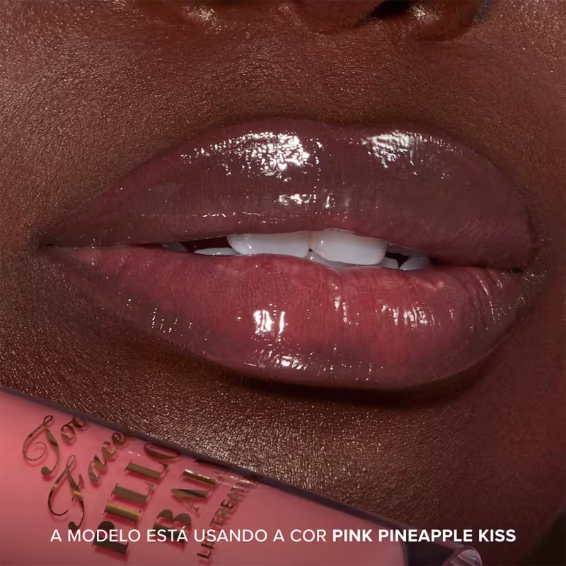 A imagem mostra o resultado do uso do Lip Treatment Too Faced Pillow Balm, com foco nos lábios. Frase: A modelo está usando a cor Pink Pineapple Kiss