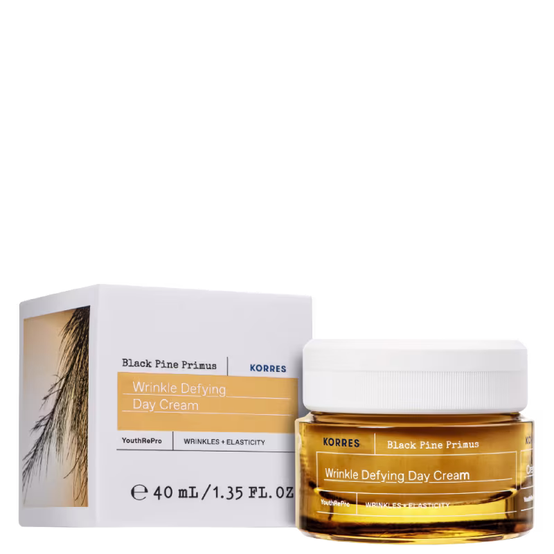 Frasco de creme facial antirrugas da marca Korres, com embalagem branca e laranja. O rótulo indica o nome do produto "Wrinkle Defying Day Cream" e a marca "Black Pine Primus".