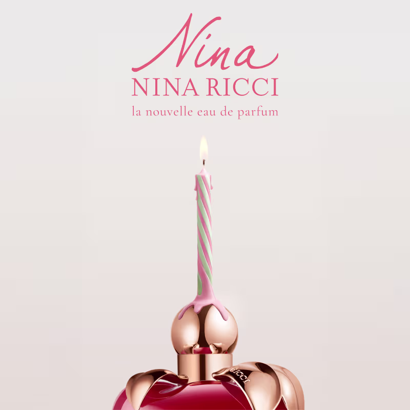 Frasco de perfume em formato de maça, com tampa dourada, em cor vermelha brilhante. Rótulo com nome da marca "Nina Ricci" visível.
