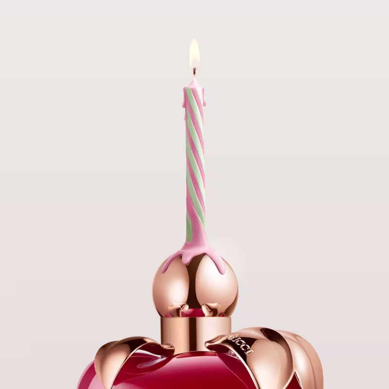 Vela de aniversário com listras rosa e verde, no topo do frasco de perfume em formato de maçã.
