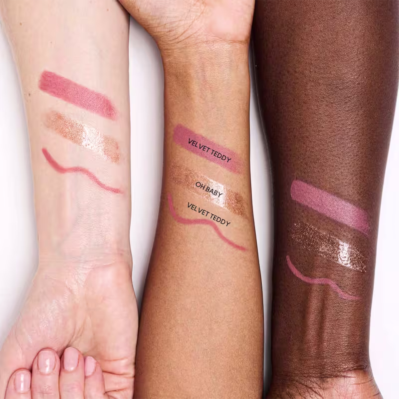 Conjunto de produtos de maquiagem da marca MAC, incluindo um batom rosa, um lápis de boca e um gloss dourado em embalagens pretas e brancas com padrões florais.