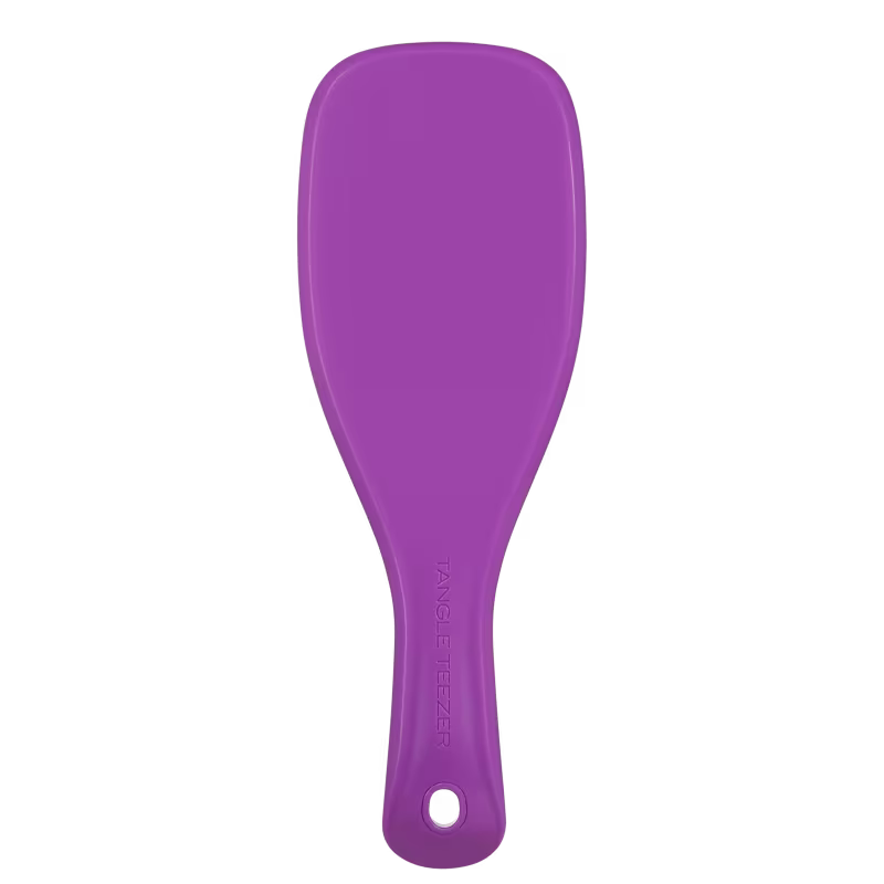 Espátula de plástico rígido de cor roxa, com o texto "Tangle Teezer" impresso na superfície. O objeto possui um formato alongado e curvo, provavelmente destinado a aplicação de produtos de beleza.