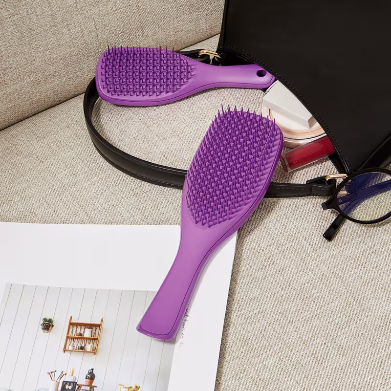 Ambiente de uso de produto de beleza da marca, com escova de cabelo e acessórios de maquiagem em uma bolsa preta sobre um fundo bege texturizado.
