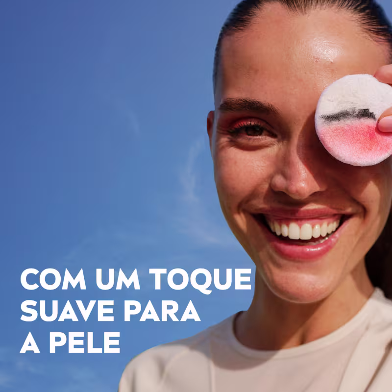 Uma mulher sorridente segura um item de perfumaria rosa com texto "Com um toque suave para a pele" visível.