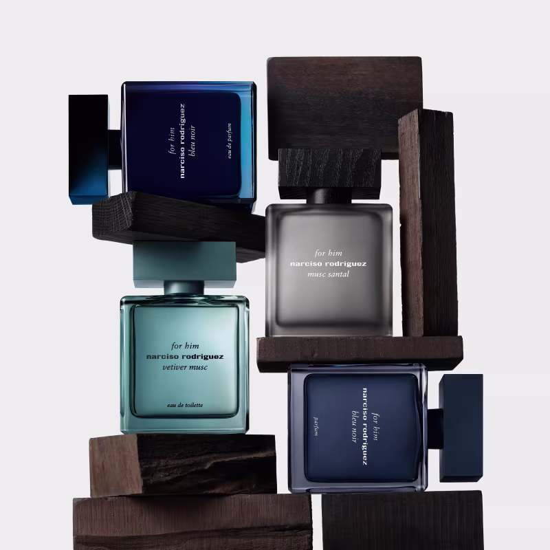 Ambiente de apresentação de fragrâncias masculinas da marca Narciso Rodriguez, com embalagens em tons azulados e madeira escura, em um cenário minimalista e elegante.