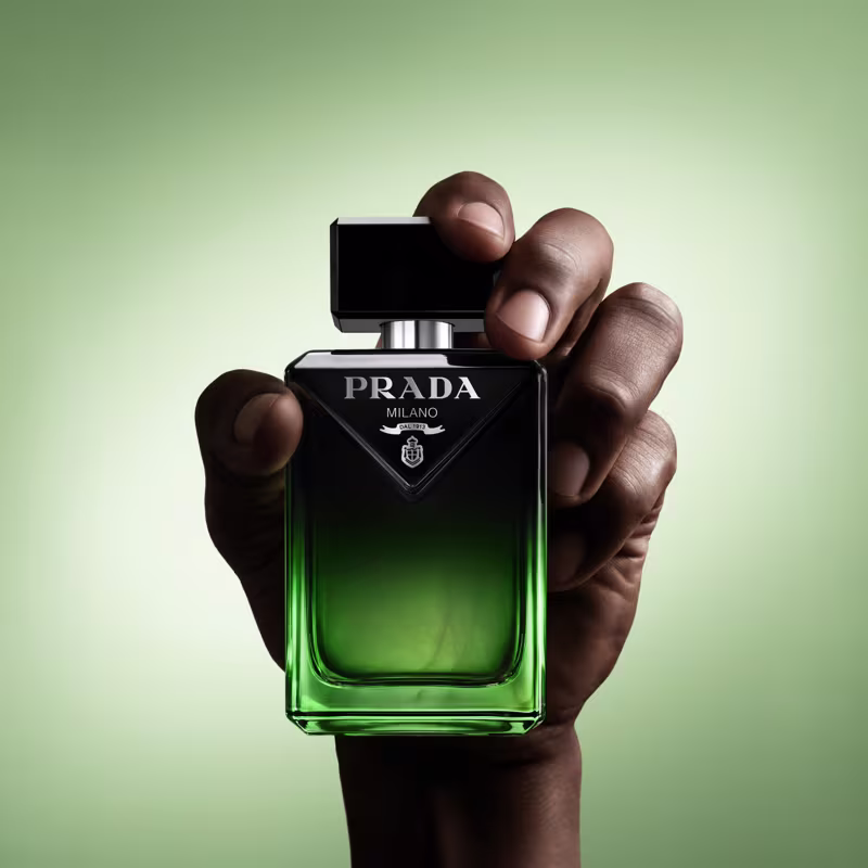 Frasco de perfume Prada Milano com design preto e verde, exibindo o logotipo da marca em destaque. O recipiente possui formato retangular com tampa preta e apresenta uma cor verde vibrante na parte inferior.