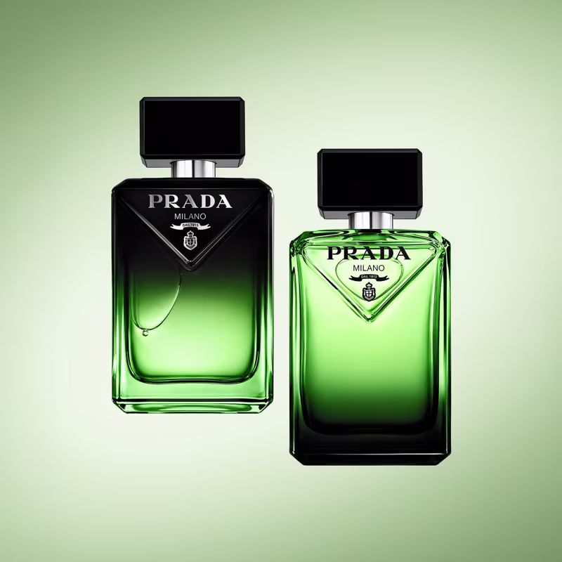 Dois frascos de perfume Prada Milano em tons de verde, com embalagens pretas e detalhes em prata. O frasco maior possui um design triangular, enquanto o menor tem um formato mais tradicional.