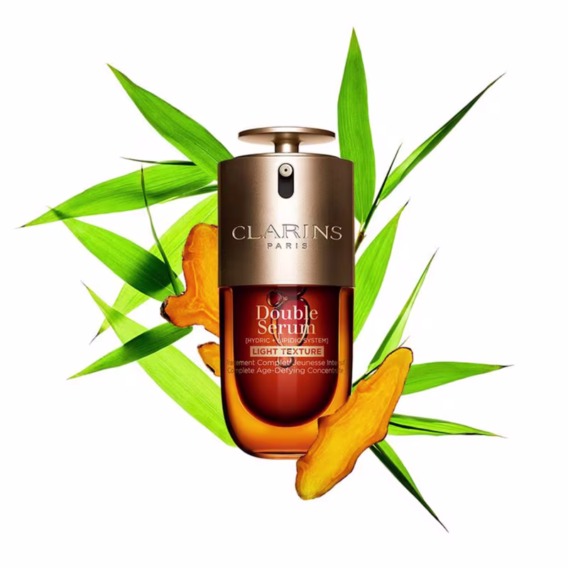 Ambiente natural com folhagem verde e flores alaranjadas destacando o frasco dourado do produto Clarins Double Serum Light Texture