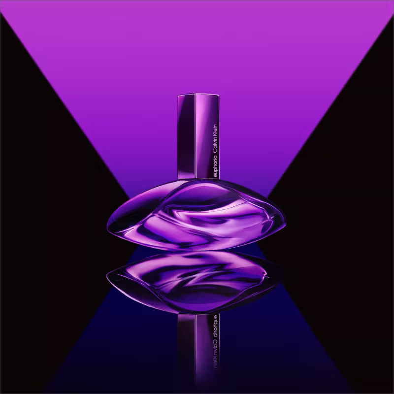 Frasco de item de perfumaria de cor violeta brilhante, com formato ovalado e tampa retangular. Rótulo com o texto "euphoria Calvin Klein" em letras brancas.