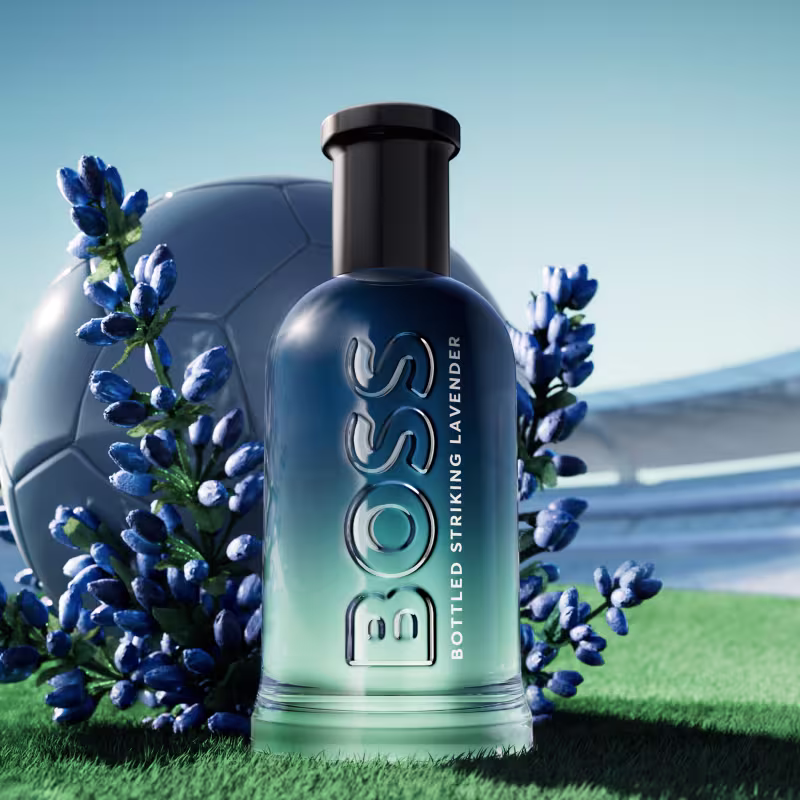 Recipiente do perfume em destaque, rodeado por botões de flores azuis e brancos em fundo degradê azul e verde. Ambiente sugere sofisticação e elegância.