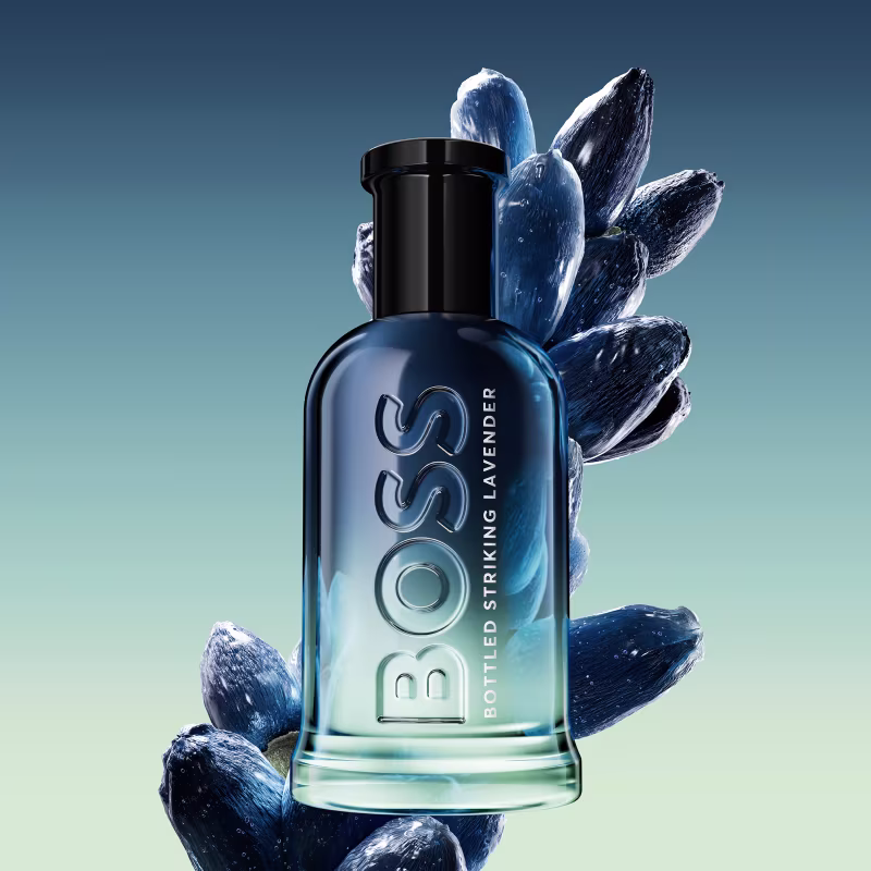 Recipiente do perfume em destaque, rodeado por botões de flores azuis e brancos em fundo degradê azul e verde. Ambiente sugere sofisticação e elegância.