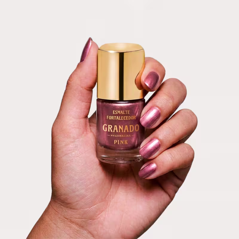 Mão segurando o frasco de esmalte da marca Granado, com tampa dourada, rótulo com texto "Esmalte Fortalecedor ".