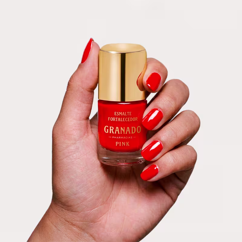 Mão segurando o fasco de esmalte da marca Granado, com tampa dourada, rótulo com texto "Esmalte Fortalecedor ".